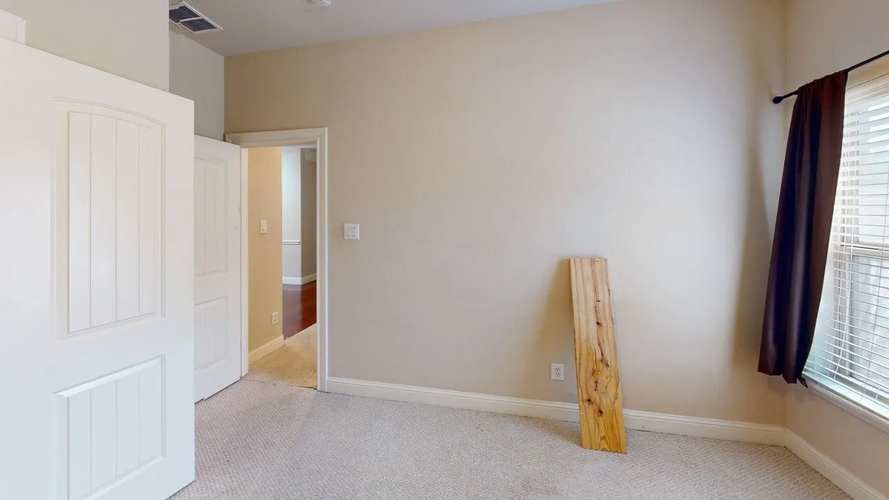 Interior room featuring neutral wall paint, light-toned carpeting, and a window with blinds