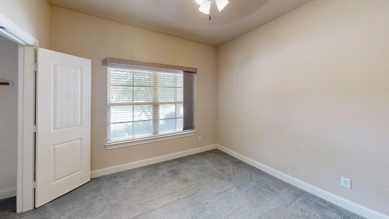 Neutral tone wall paint, textured gray carpeting, white trim work, white paneled interior door, and a ceiling fan with light fixture