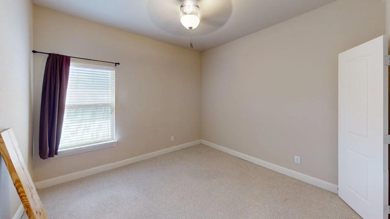 Neutral wall color, light-toned carpet flooring, window with blinds, panel door, and ceiling light fixture