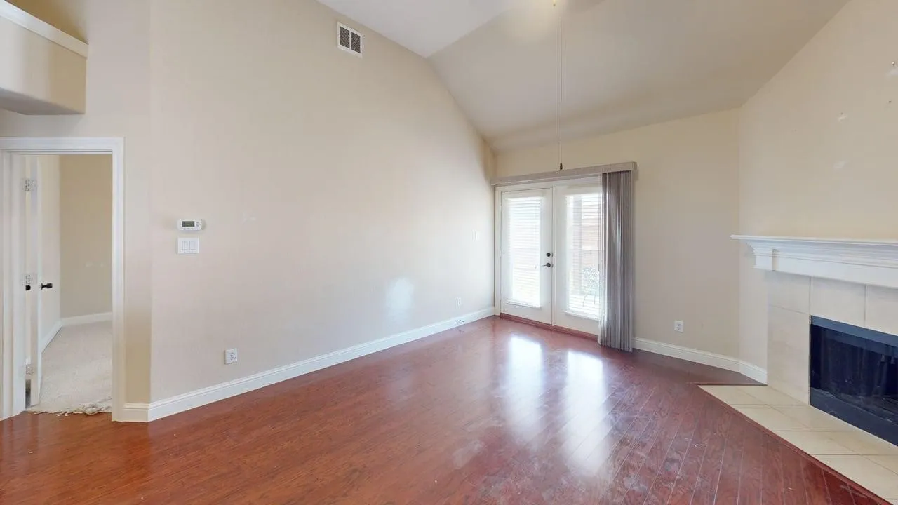 Vaulted ceiling, wood-finish flooring, white trim details, fireplace with tile surround, and double French doors