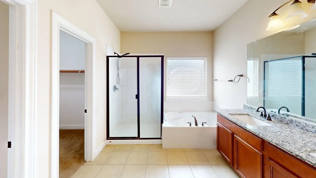 Tile flooring, dual vanity with granite countertop, built-in soaking tub, separate shower with glass enclosure, and a walk-in closet
