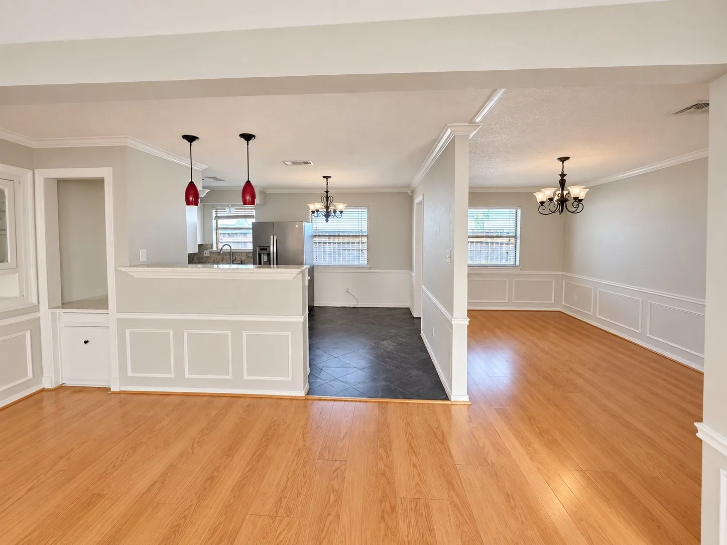 Wood-finish flooring throughout, wainscoting details, built-in cabinetry, modern pendant lighting, and a stainless steel refrigerator