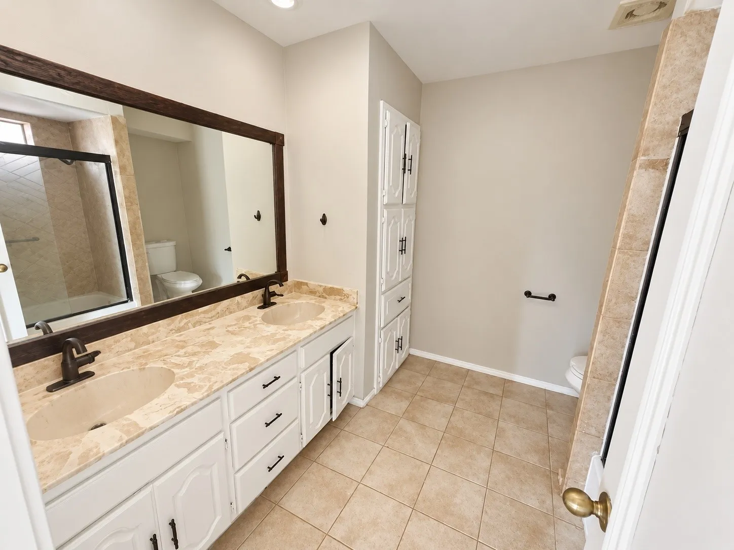 Double vanity with dual undermount sinks, stone-finish countertop, and bronze-finish faucets