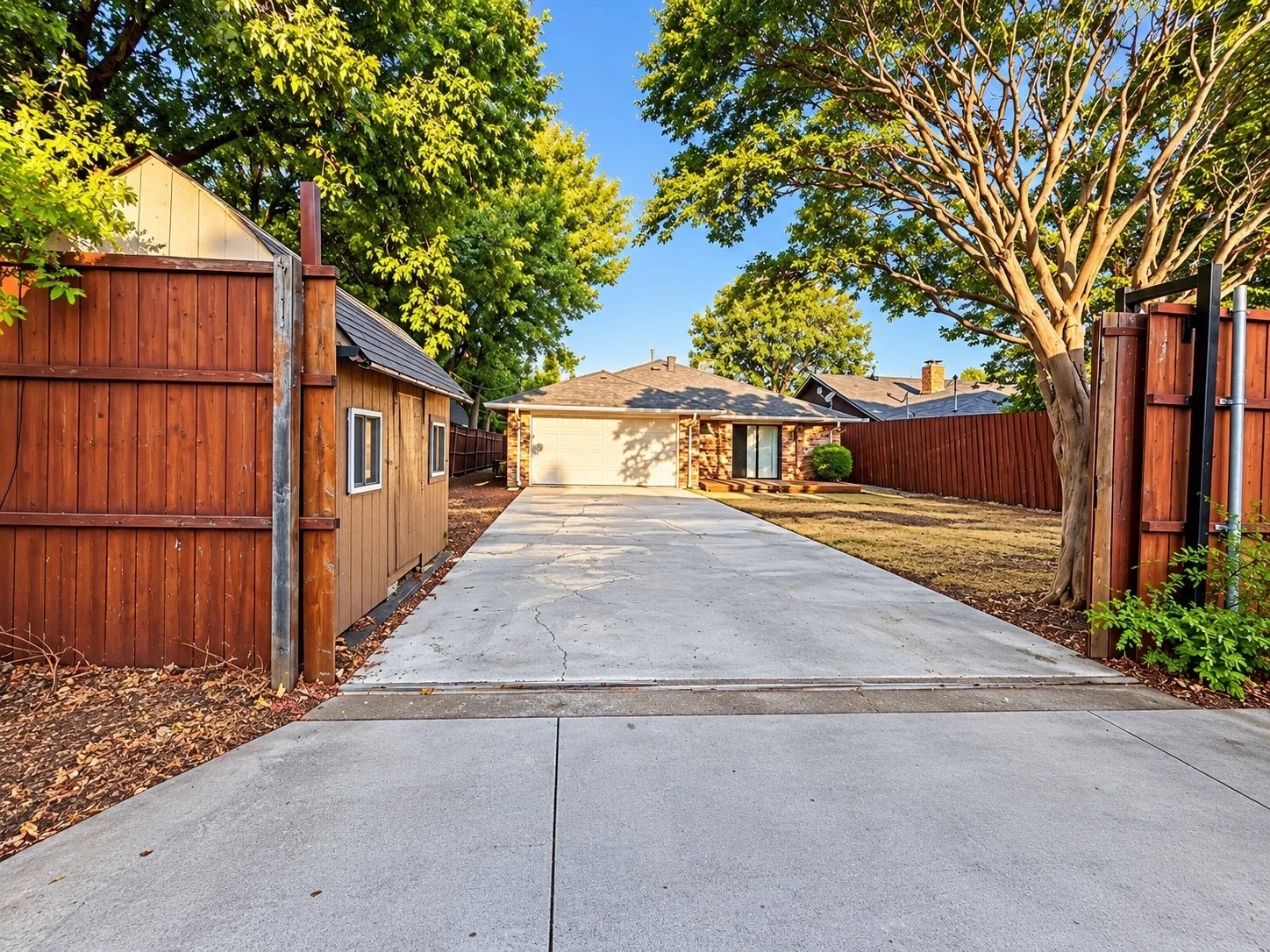 Extended concrete driveway, wood privacy fencing, stone exterior, detached wood shed, and mature trees