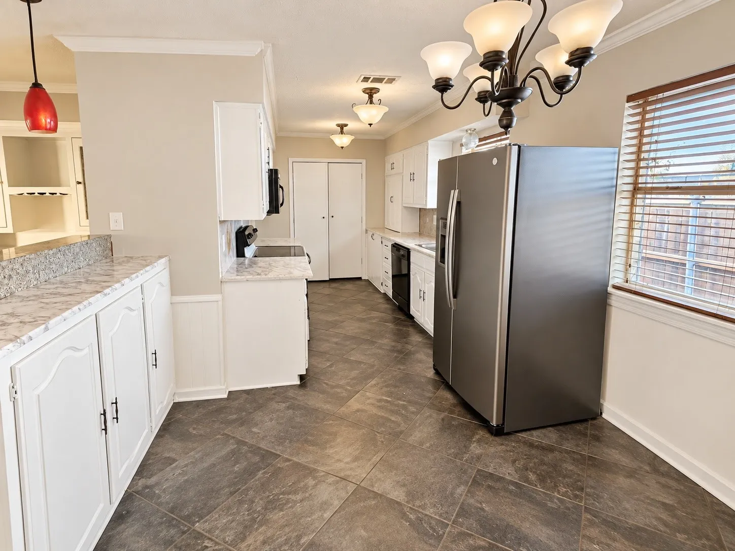 Kitchen featuring white cabinetry, stone-finish countertops, stainless steel refrigerator, tile flooring, and a decorative chandelier