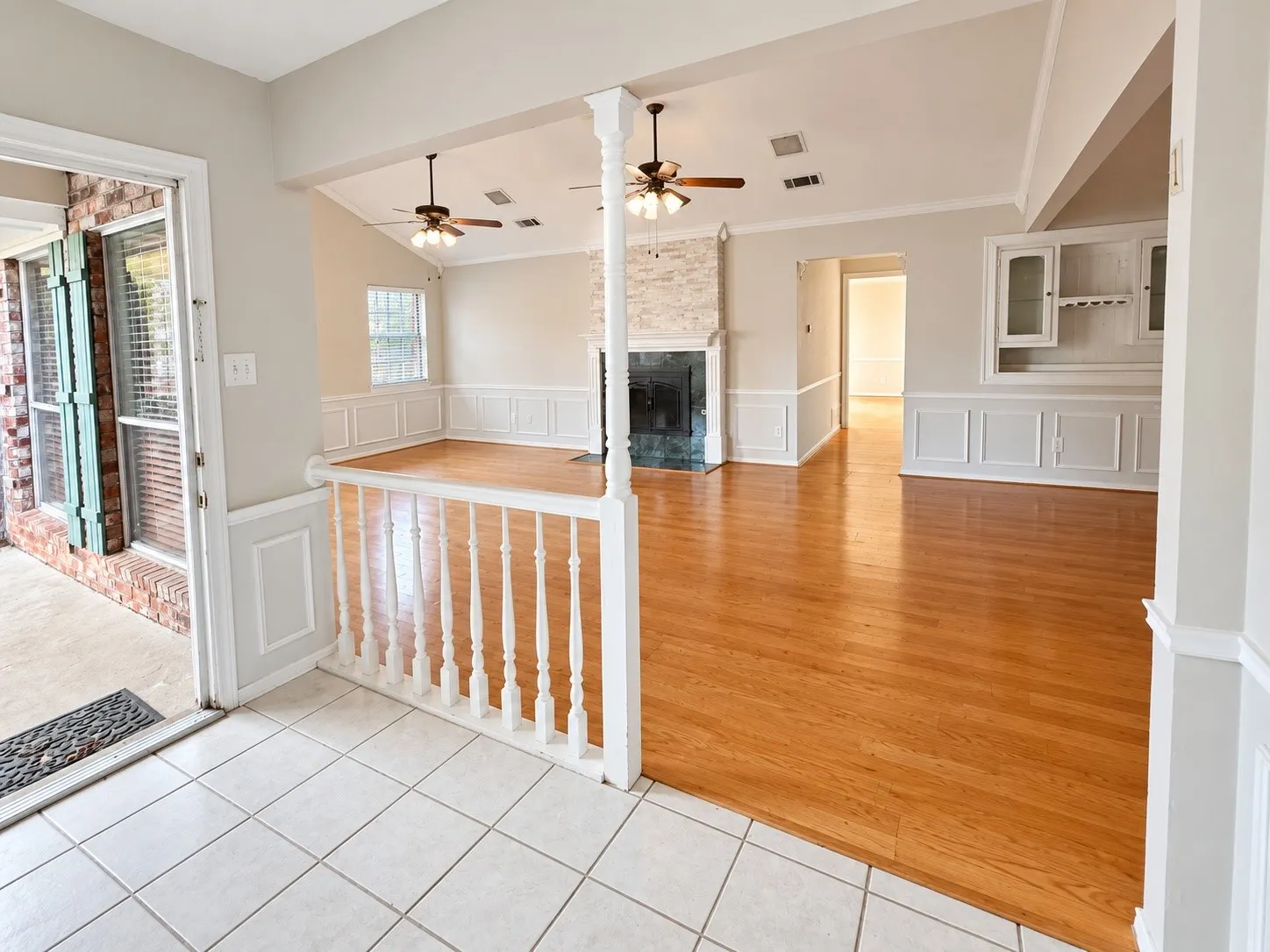Hardwood flooring throughout the main living area, fireplace with stone surround, wainscoting details, built-in display cabinetry, and ceiling fans