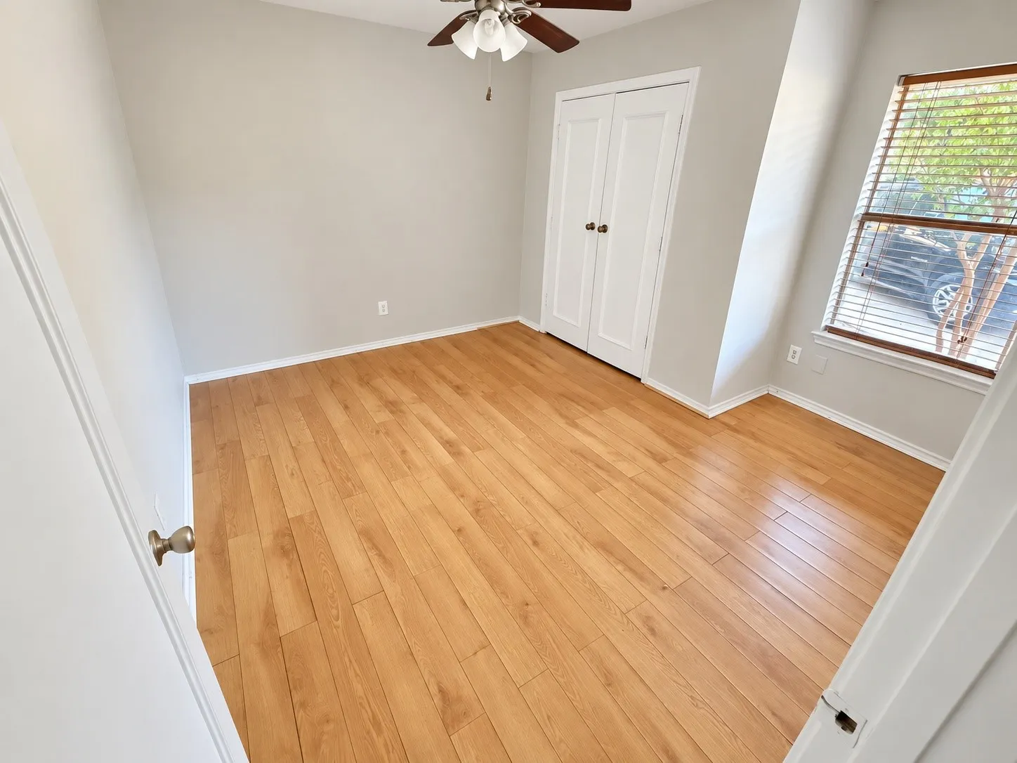 Wood-finish flooring with light gray walls, white trim, and a window with blinds