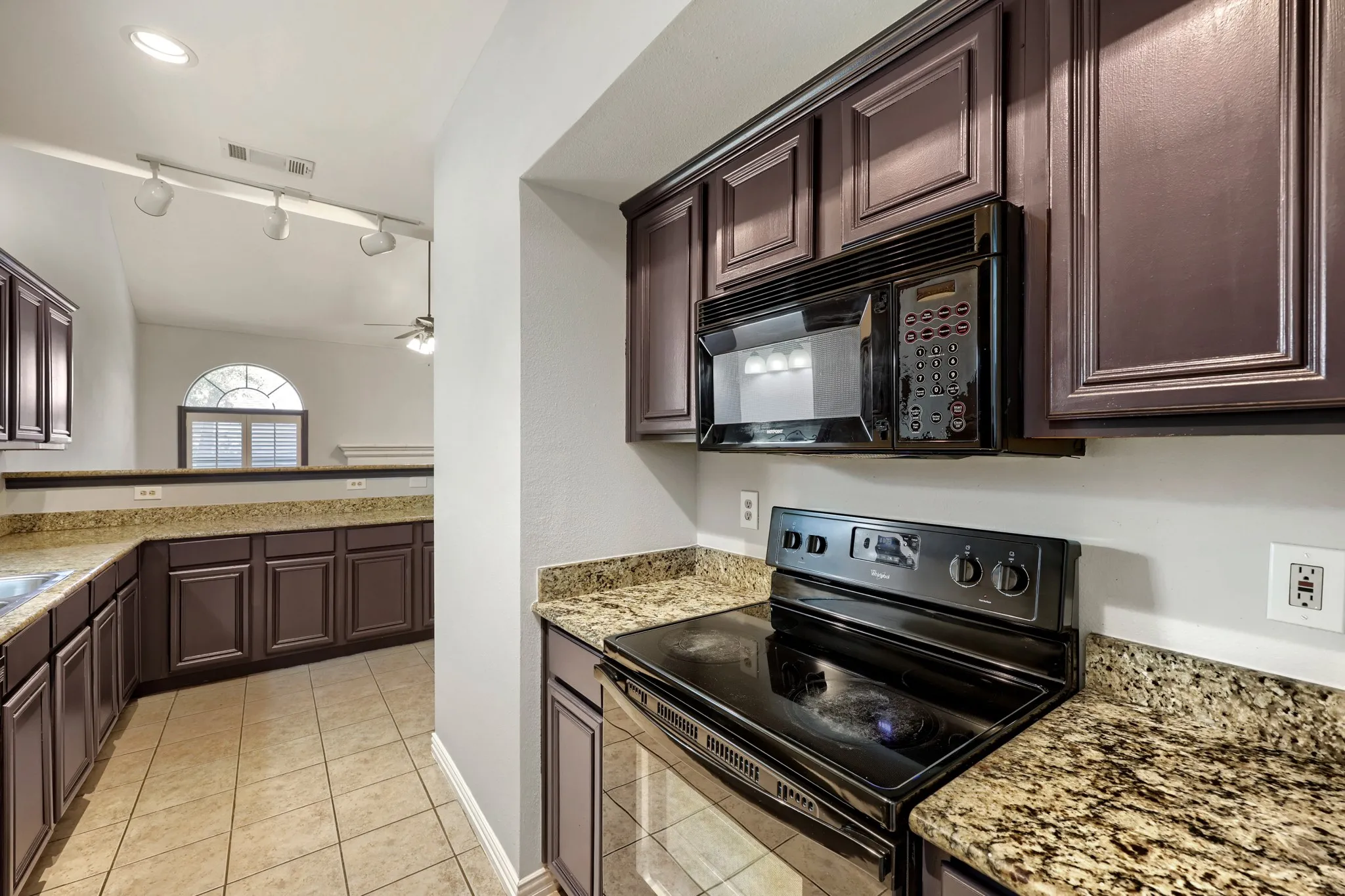 Kitchen with dark wood cabinetry, granite-style countertops, tile flooring, and integrated black appliances