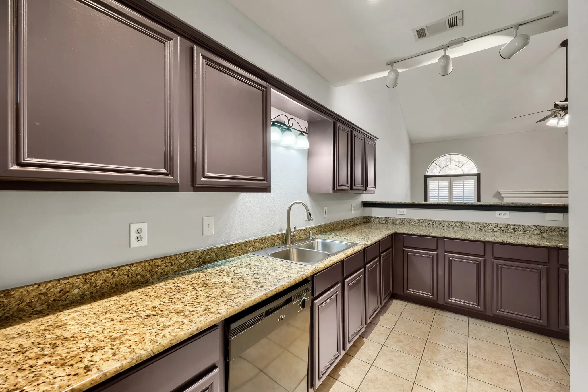 Kitchen featuring brown cabinetry, stone countertops, stainless steel sink, and tile flooring
