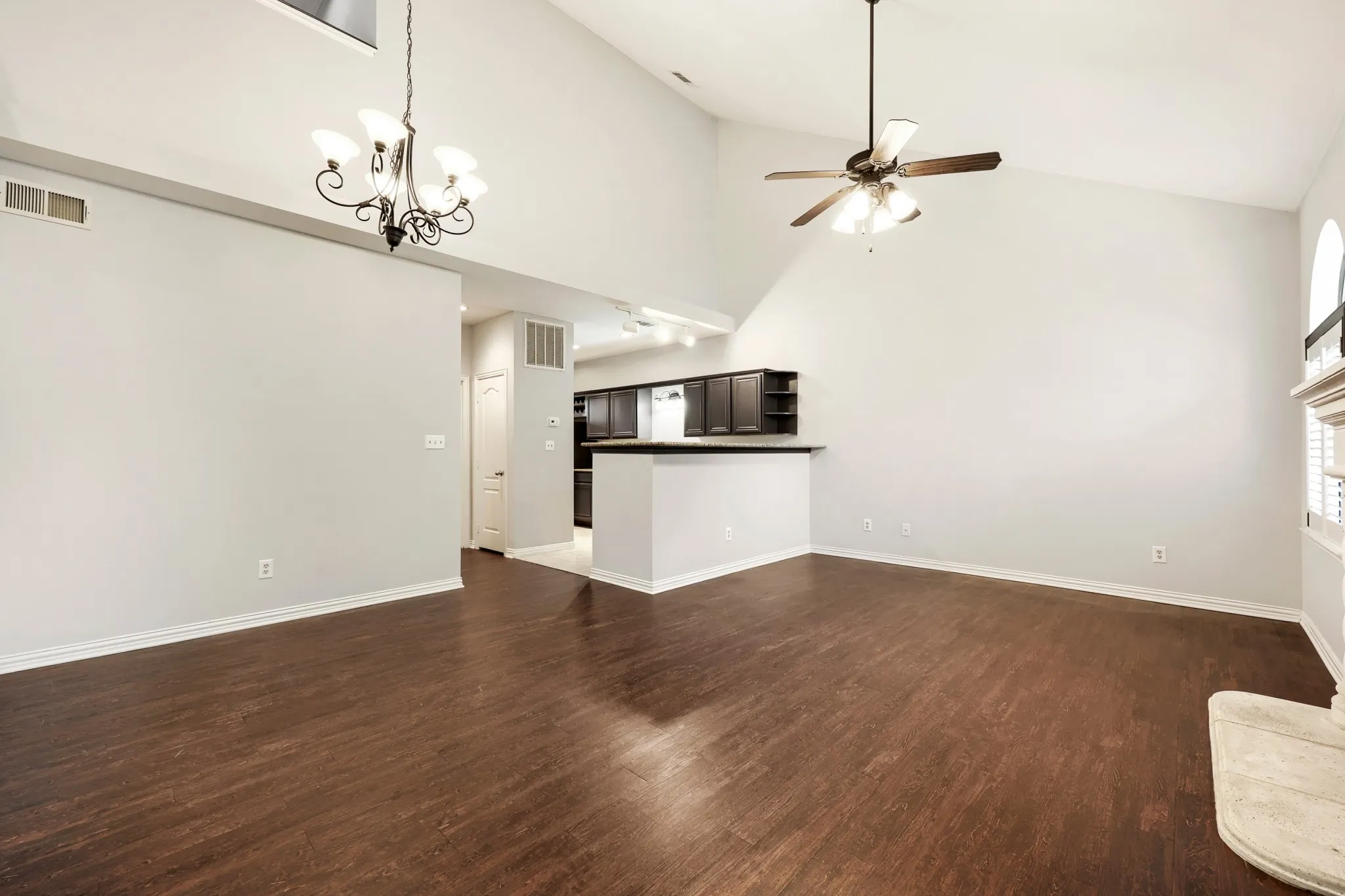 Vaulted ceilings with a chandelier and ceiling fan, wood-finish flooring, and a fireplace with a mantel
