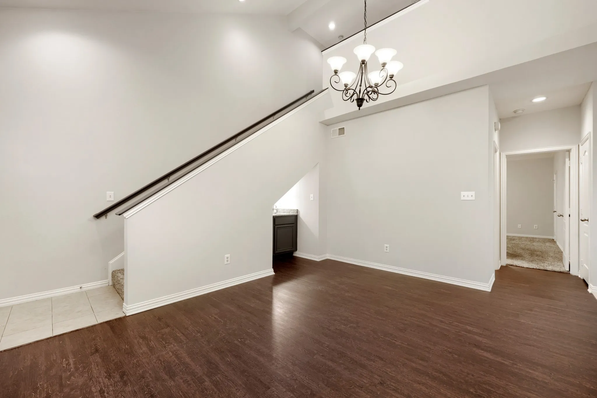 High ceilings with a decorative chandelier, wood-finish flooring, a built-in wet bar, recessed lighting, and a staircase with a dark wood handrail