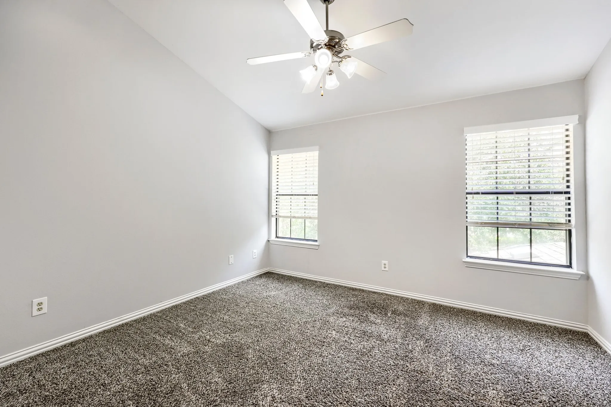 Vaulted ceiling, ceiling fan with light fixture, two windows with blinds, and textured carpeting