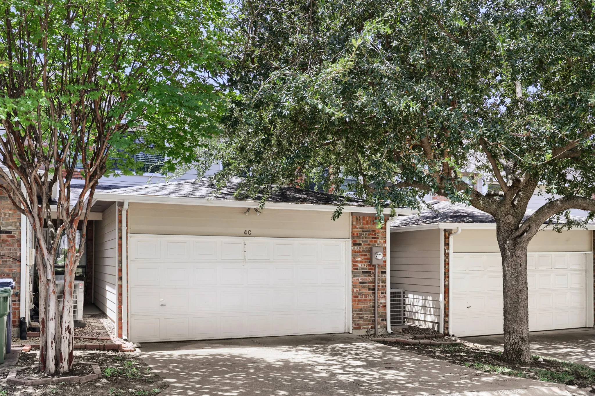 Exterior featuring brick and siding finishes, two integrated garage doors, and mature trees providing shade