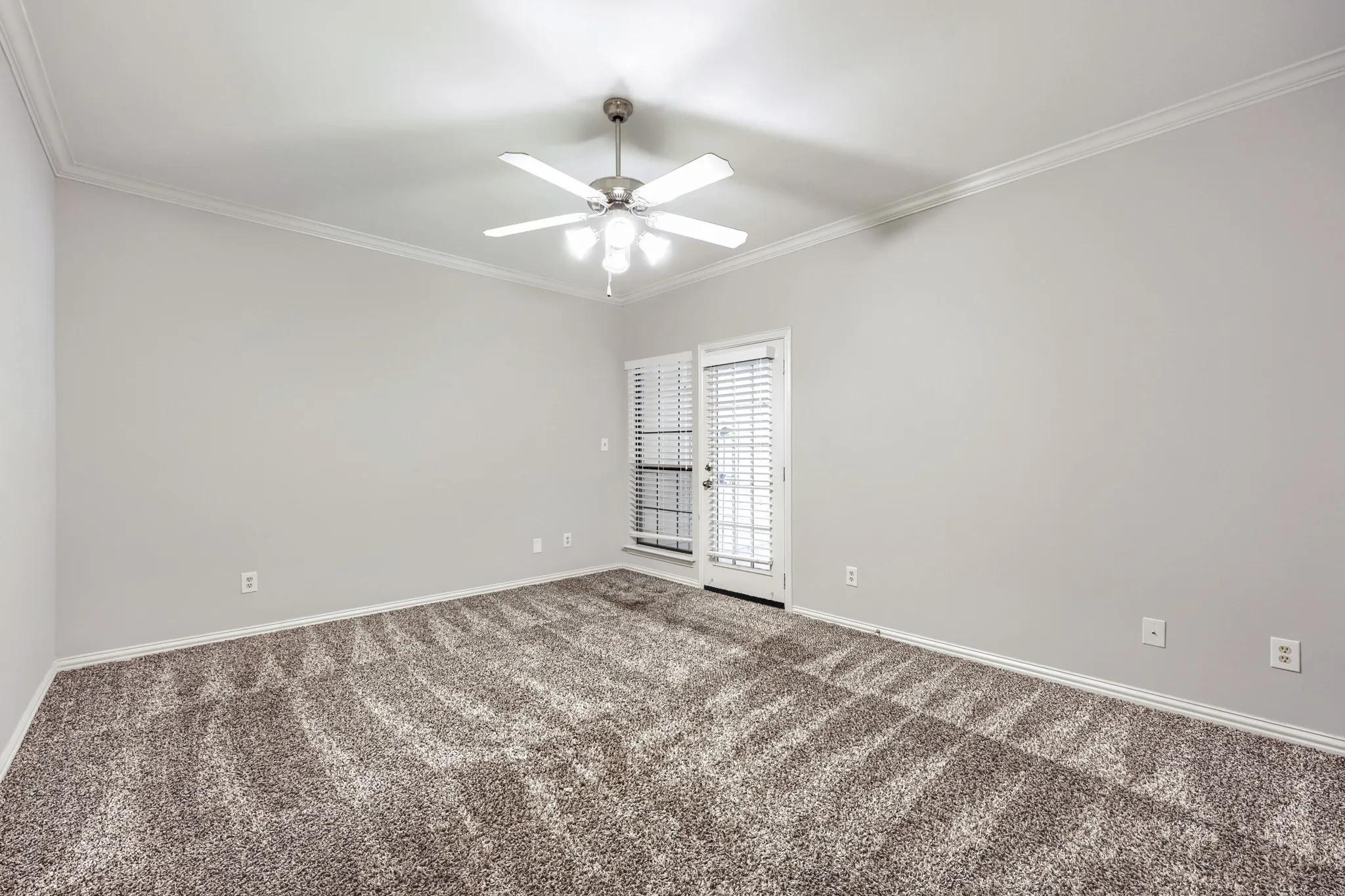 Spacious room featuring neutral paint, crown molding, patterned carpet, a ceiling fan with integrated lighting, and a white door with integrated blinds