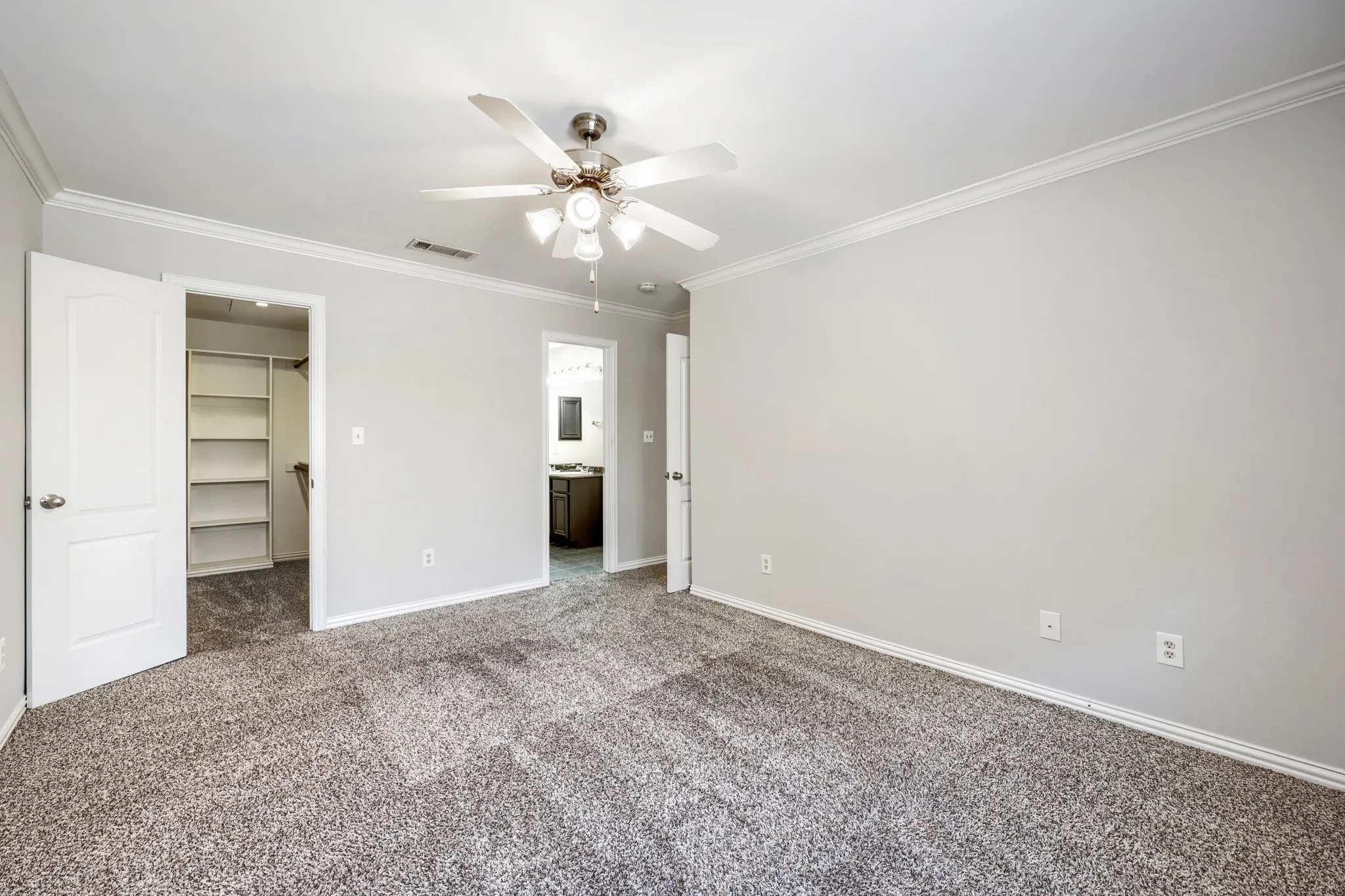 Spacious room with gray textured carpet, white walls, crown molding, and a ceiling fan with integrated lighting