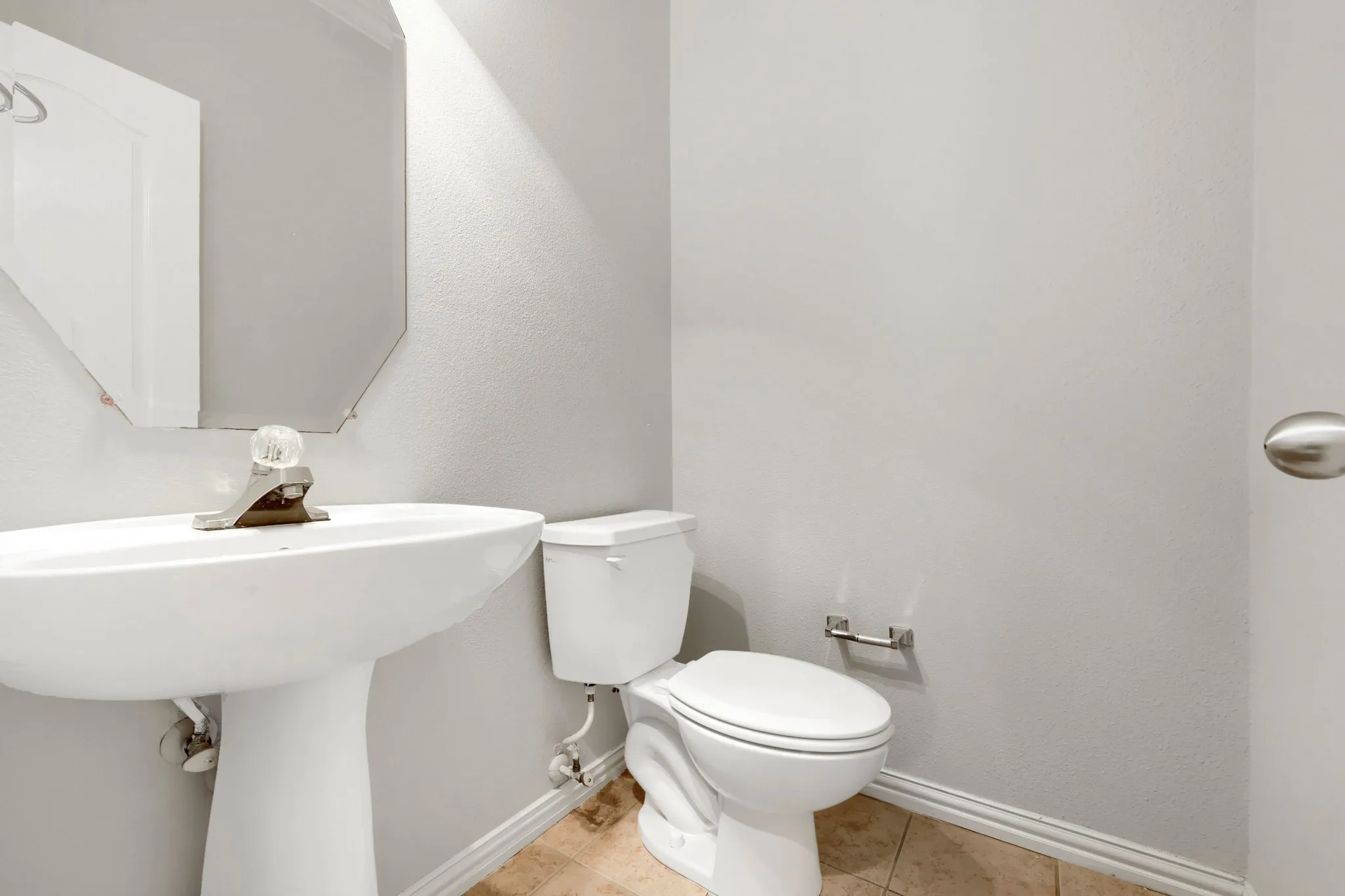 Pedestal sink with chrome faucet, toilet, and tile flooring