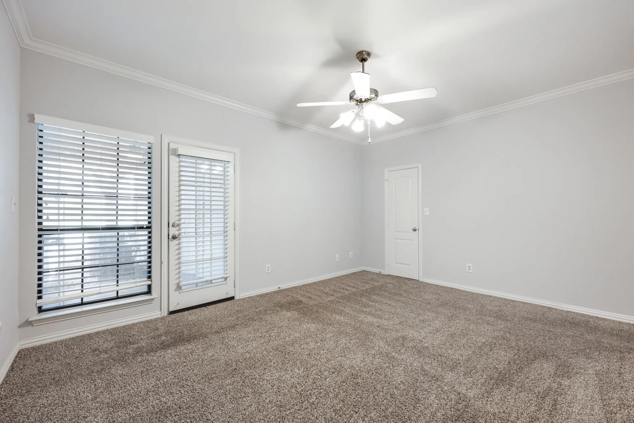 Spacious room featuring neutral carpet, crown molding, a ceiling fan with integrated lighting, and a glass-paneled door