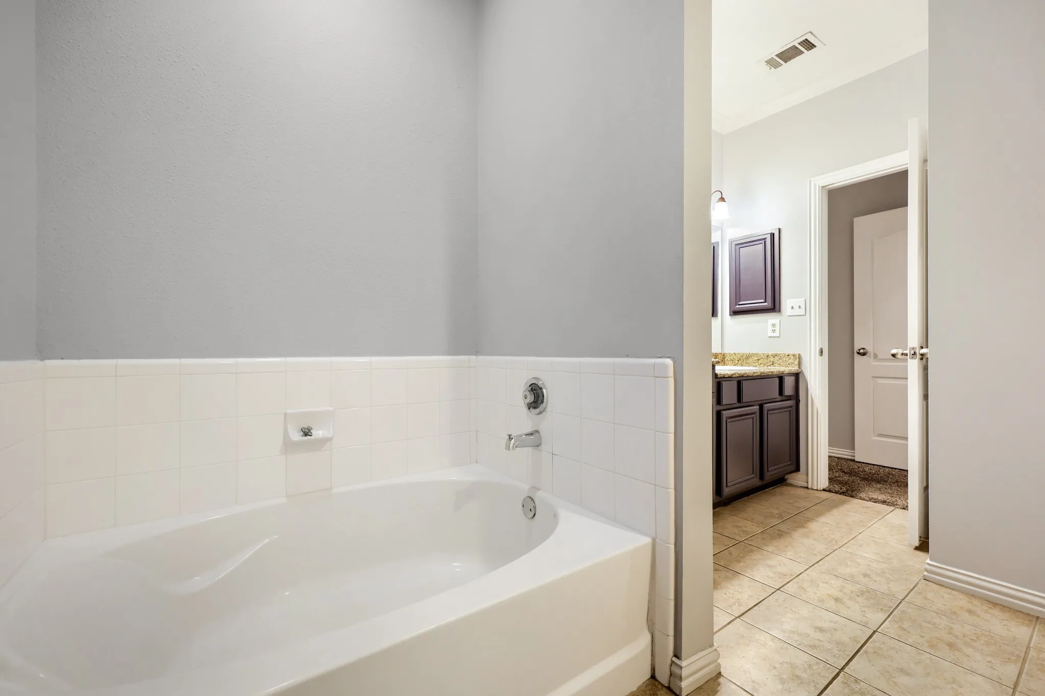 Built-in soaking tub with white tile surround, chrome fixtures, and neutral wall paint