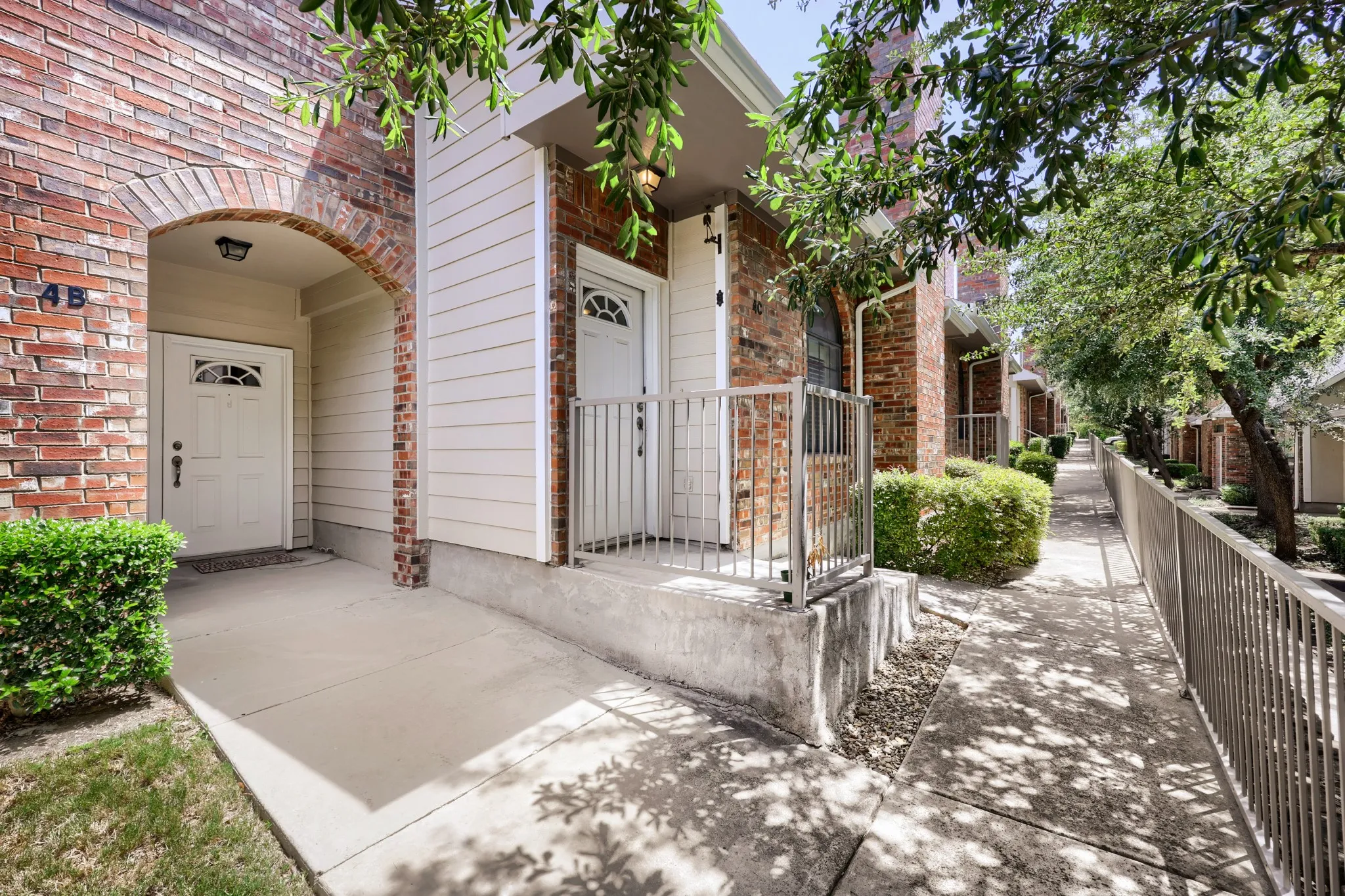 Brick and siding exterior, arched entryway, concrete walkway, metal railings, and landscaped shrubbery
