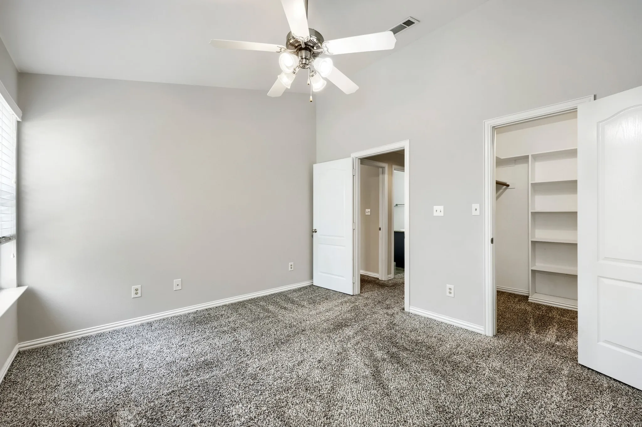 Vaulted ceiling with a ceiling fan, light gray wall paint, gray carpet flooring, a window with blinds, and a closet with shelving
