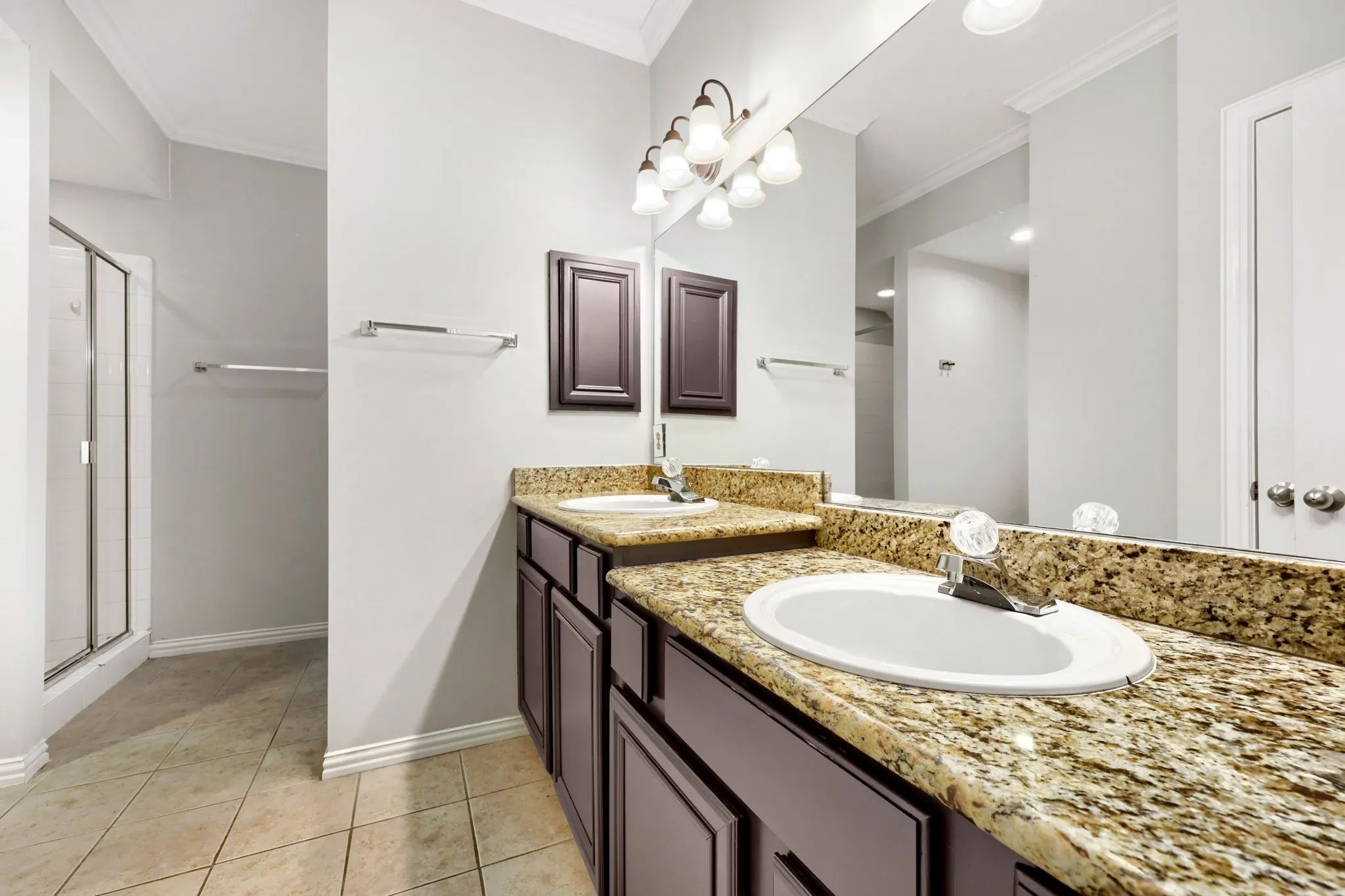 Dual vanity with granite countertops, integrated sinks, a chrome faucet, custom cabinetry, and large wall-mounted mirror
