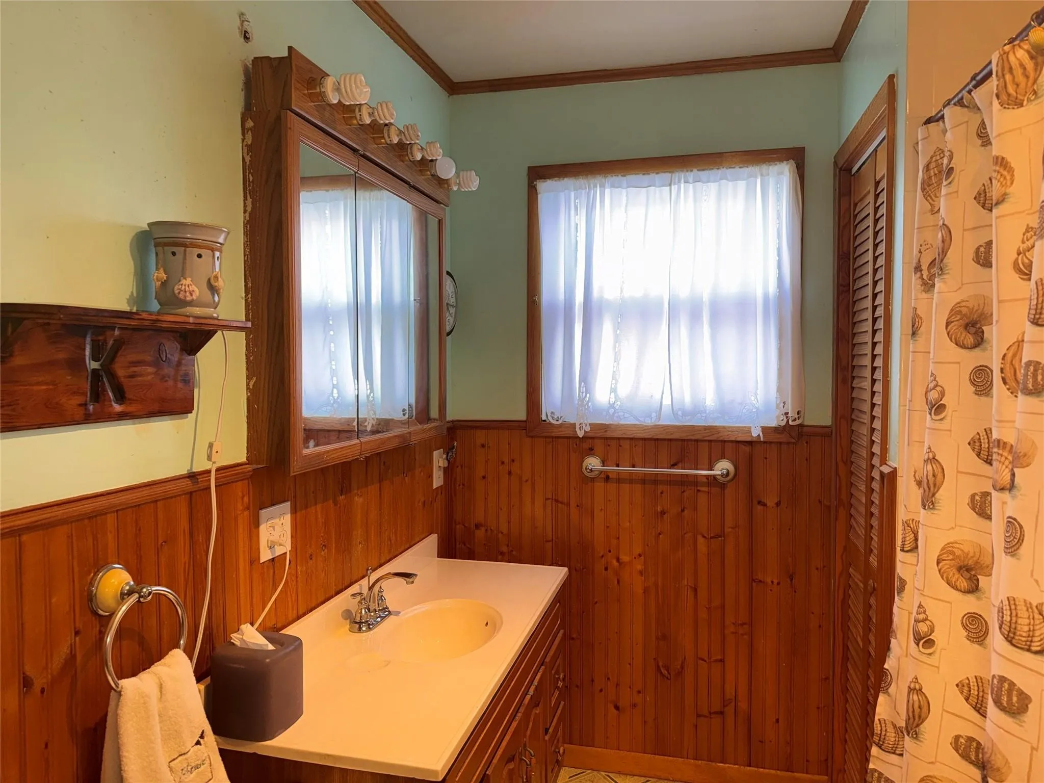 Wood paneling, a vanity with an integrated sink, a mirrored medicine cabinet, and a window with a valance