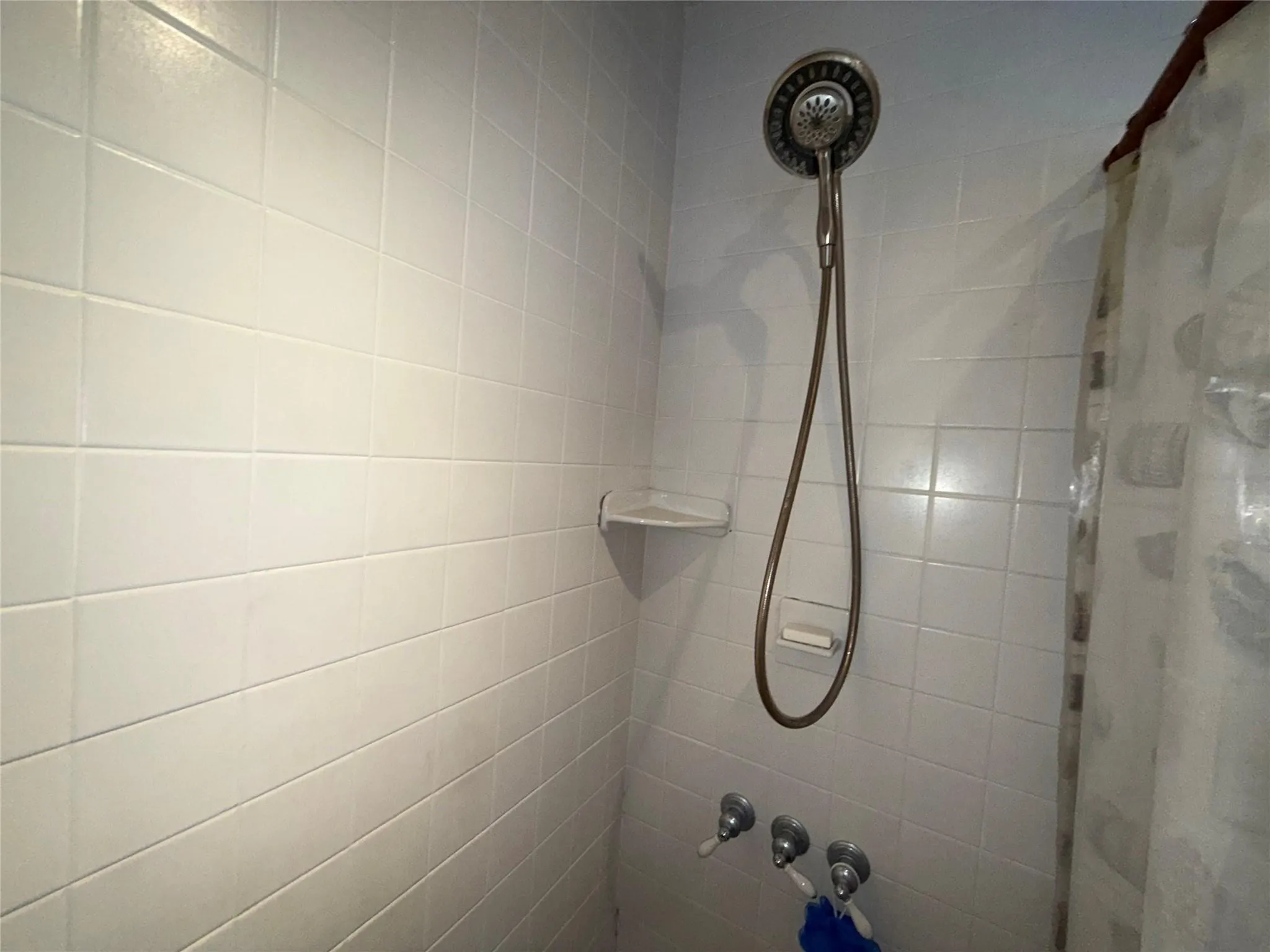 White tiled shower enclosure with a handheld showerhead, wall-mounted soap dish, and an integrated corner shelf