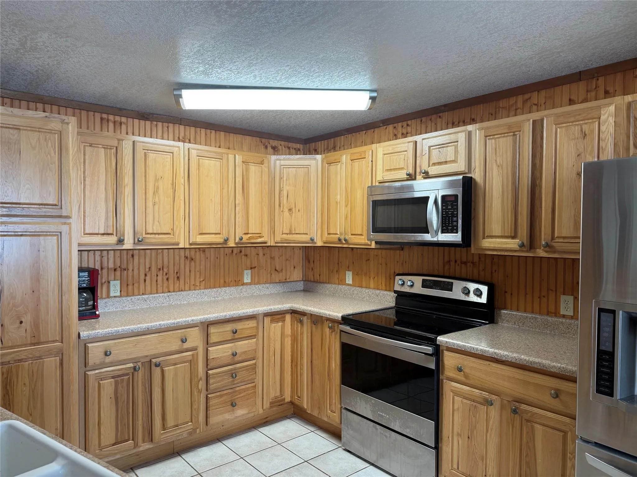 Wood-finish cabinetry with brass hardware, speckled countertops, stainless steel appliances, and tiled flooring