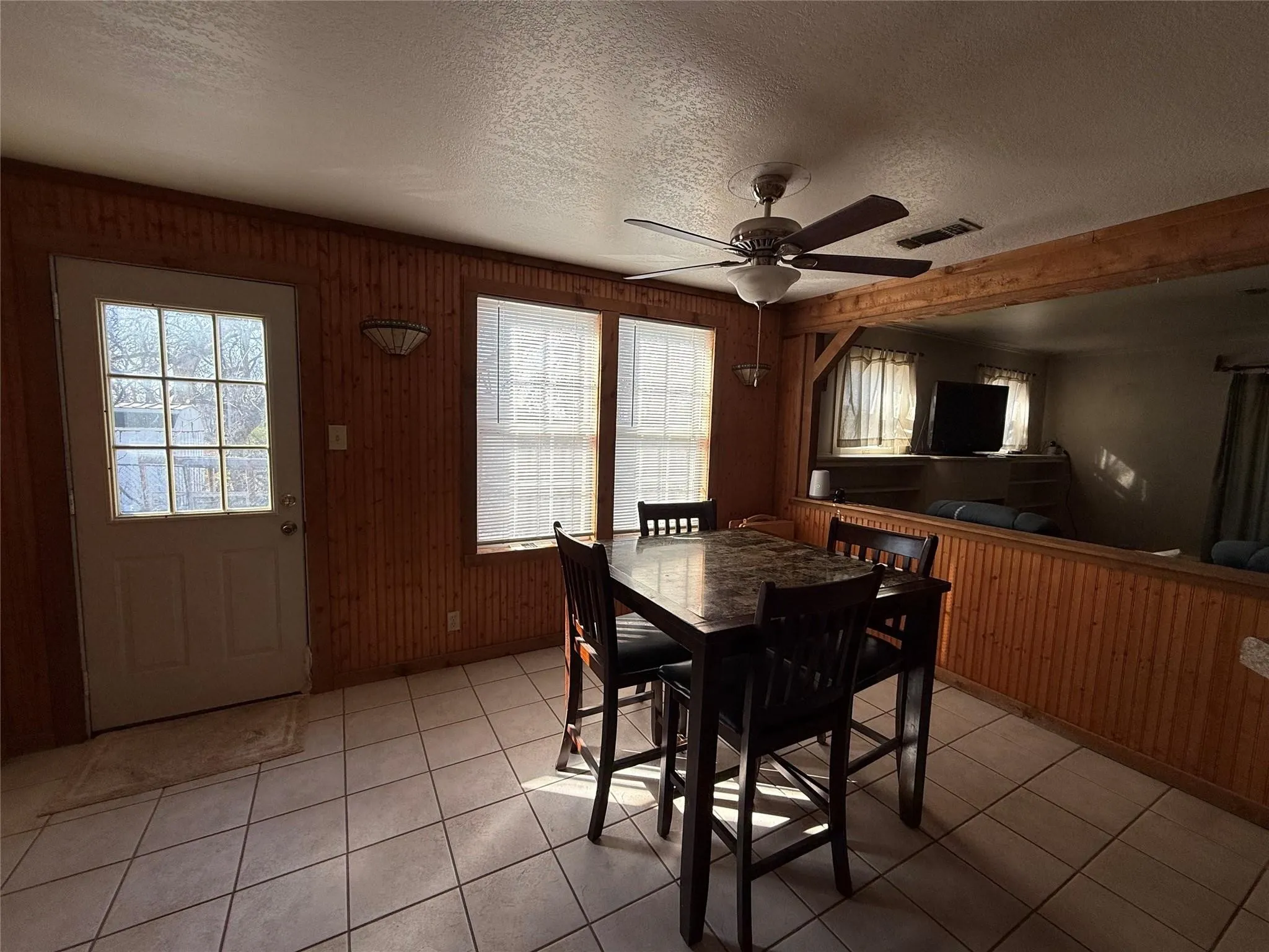 Tiled flooring, wood paneling, ceiling fan, transom window door, and exposed wood beam