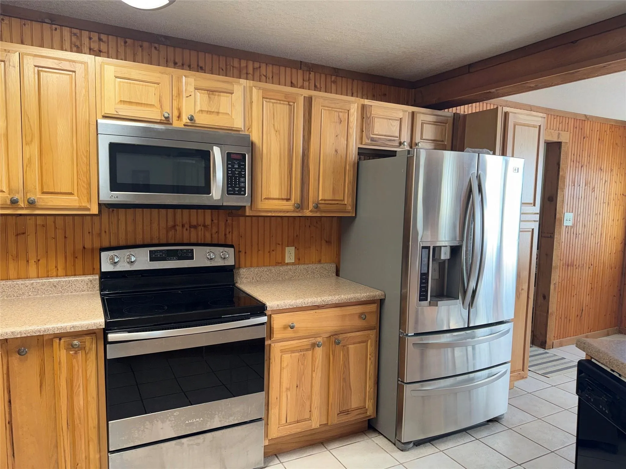 Kitchen featuring wood-finish cabinetry, stainless steel appliances, light-toned countertops, and paneled wood-finish walls