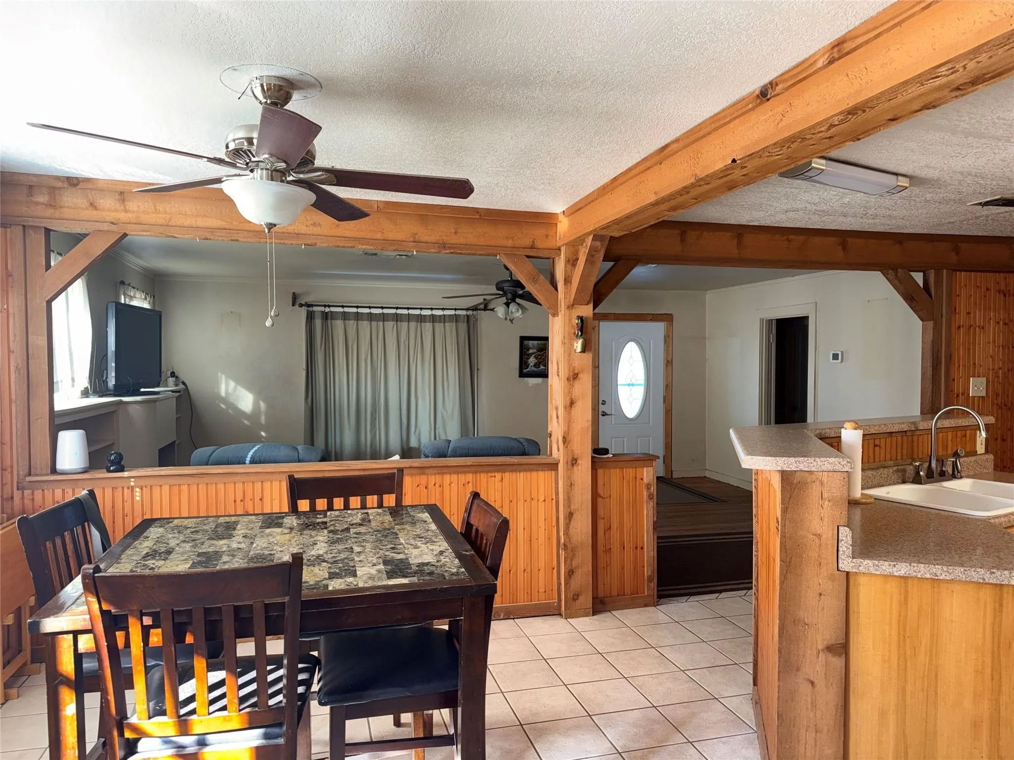 Exposed wood beams, tiled flooring, wood-paneled walls, built-in kitchen sink, and ceiling fans