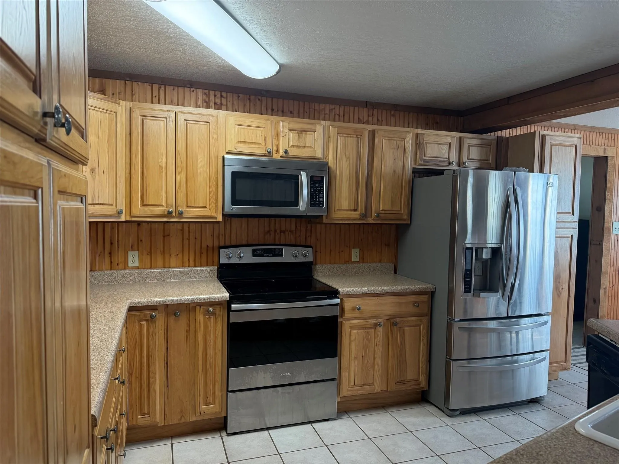 Wood-finish cabinetry paired with a wood-panel backsplash, stainless steel appliances, and tile flooring