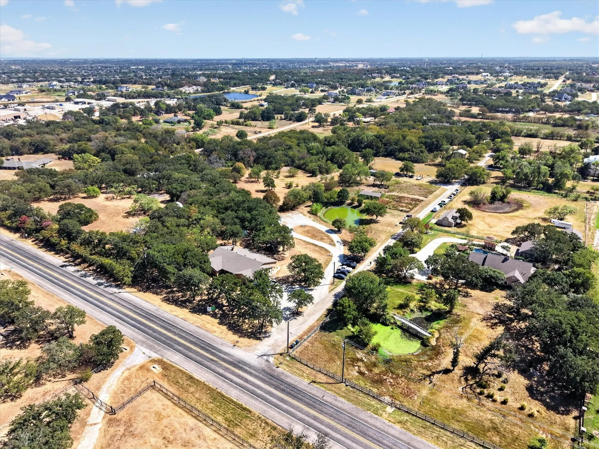 Expansive perspective showcasing the property, pond, mature trees, road frontage, and surrounding area.