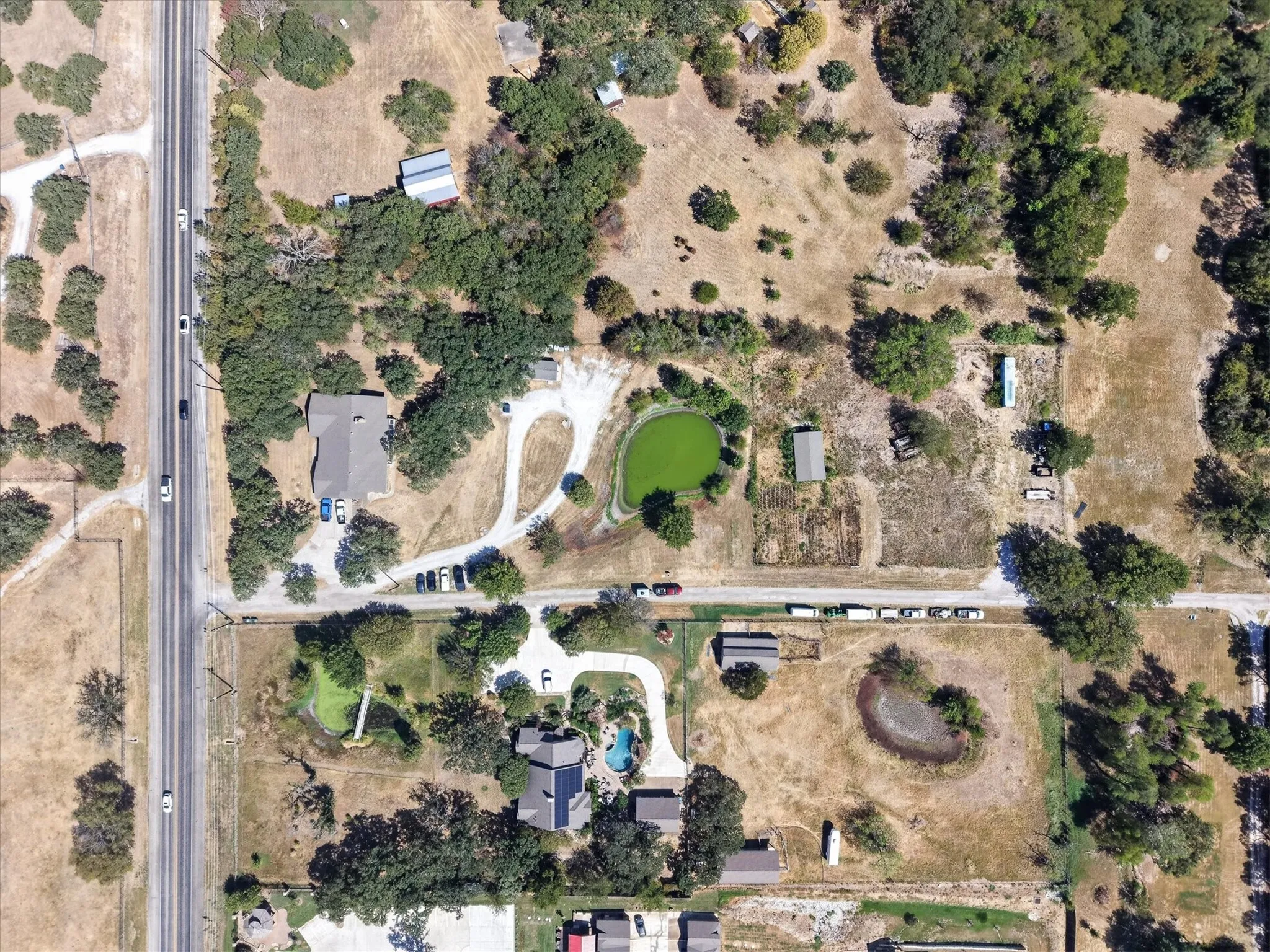 Aerial view highlighting the pond, open grounds, mature trees, and interior drive.