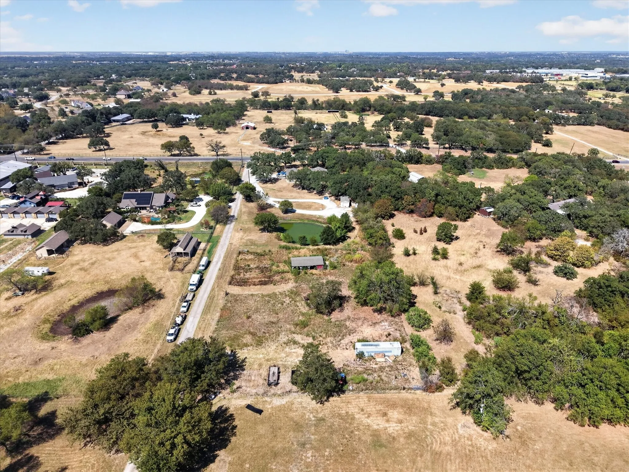 Expansive aerial view highlighting open acreage, mature trees, and pond.