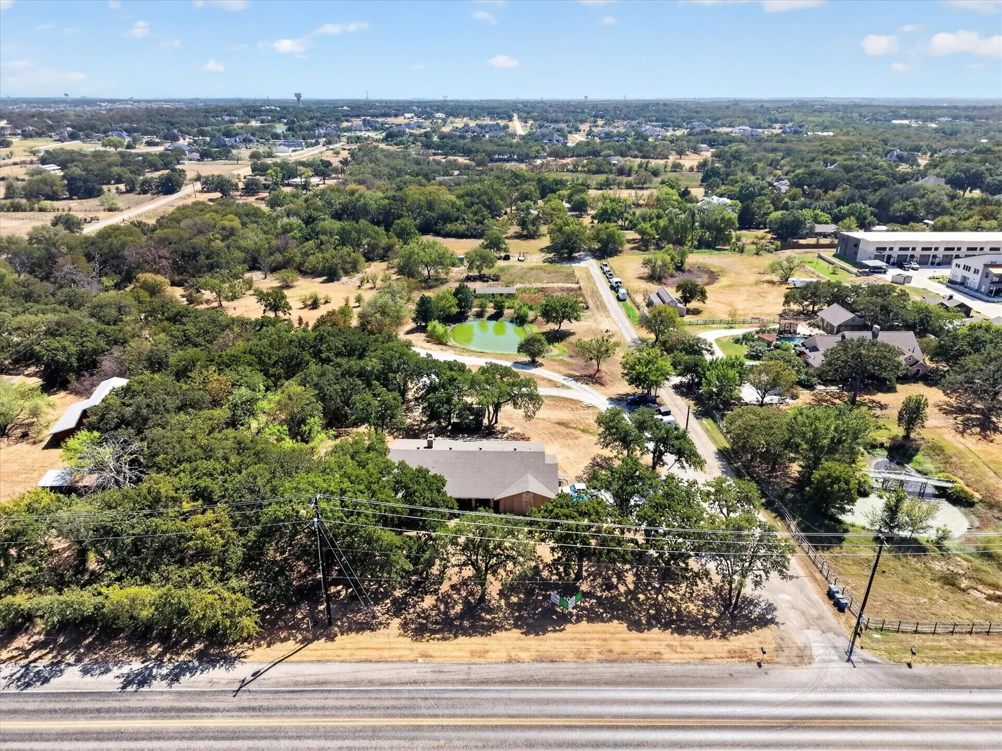 Aerial view showcasing the property, mature trees, pond, and road frontage.