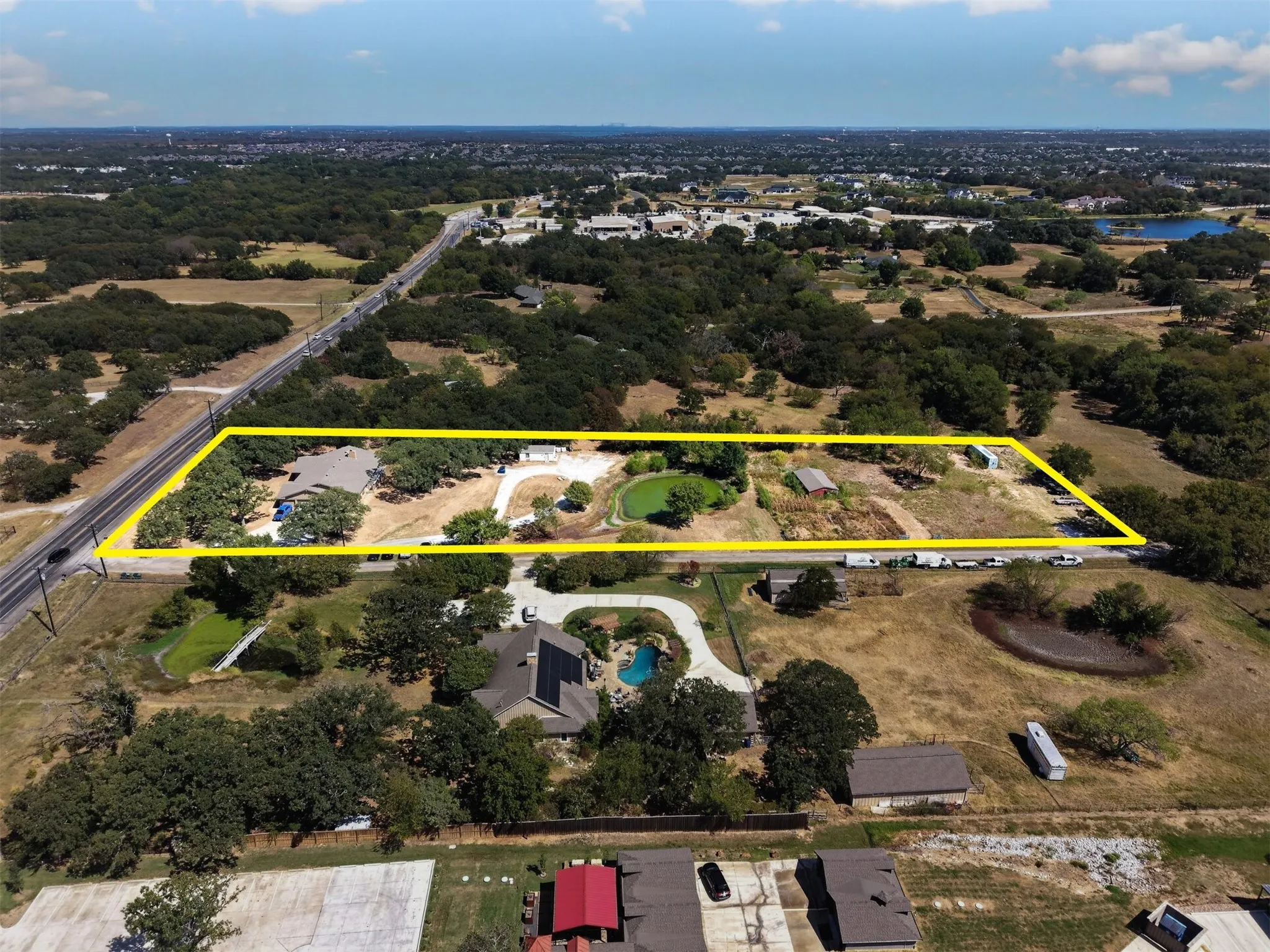 Expansive property view featuring the pond, open acreage, mature trees, existing improvements, and direct FM 407 access.