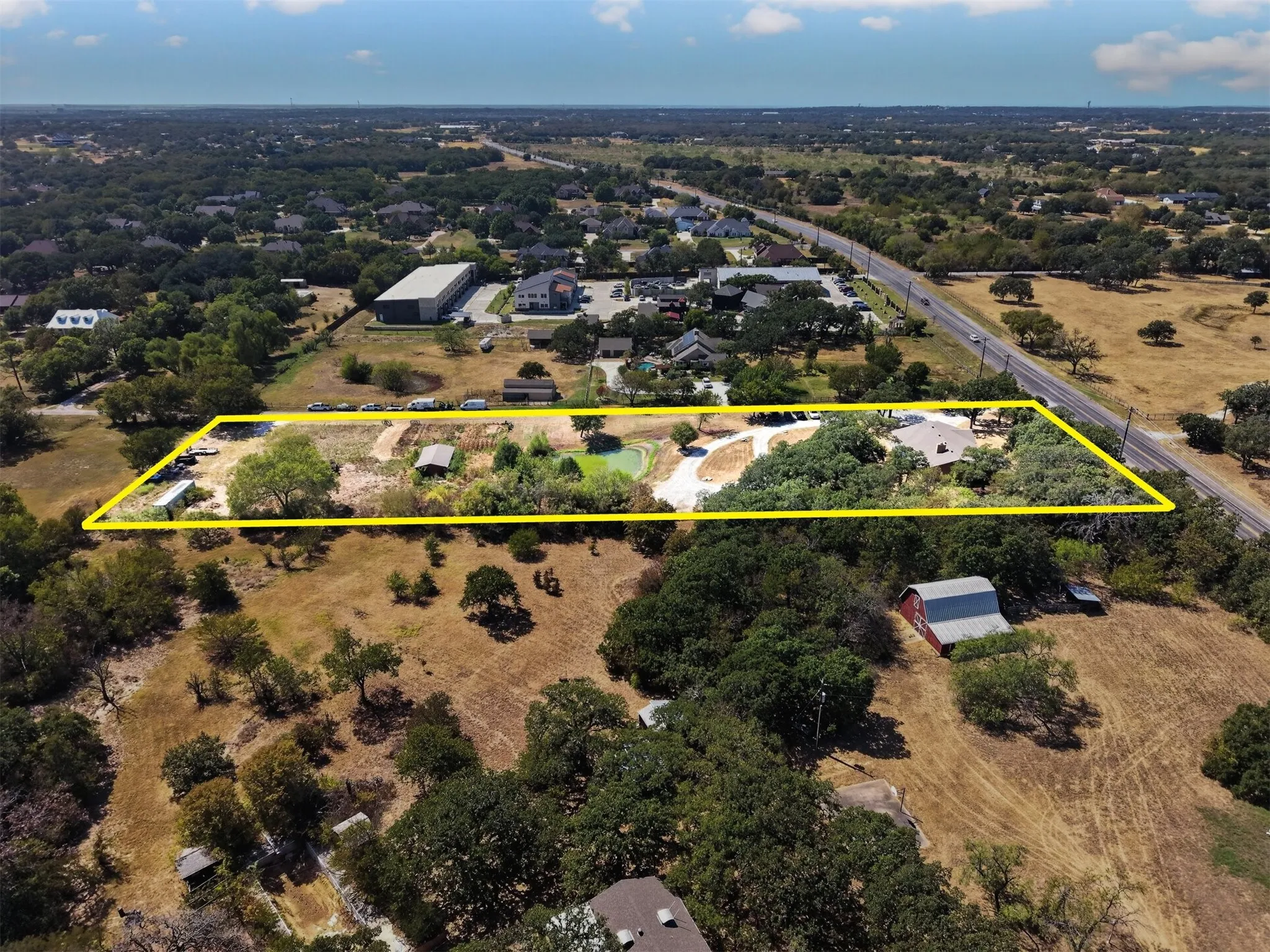 Wide perspective highlighting the depth of the property, pond, existing improvements, and nearby residential and commercial development.