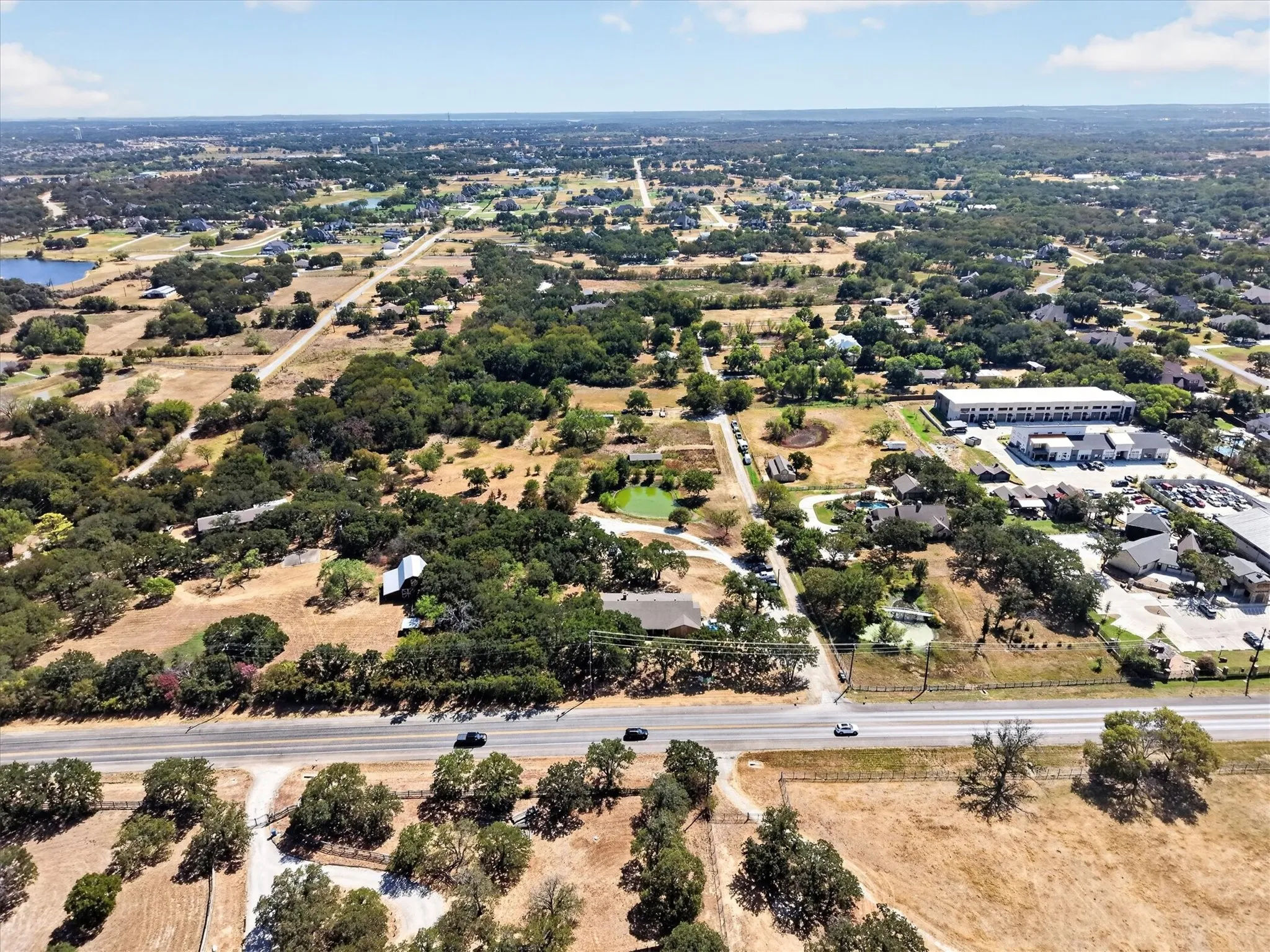 Aerial view from the roadway showcasing the property, pond, mature trees, and surrounding landscape.