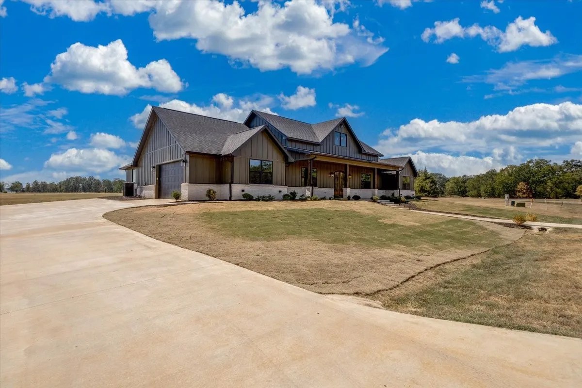 Modern farmhouse exterior with board and batten siding, stone accents, dark-framed windows, a covered front porch, and an attached garage