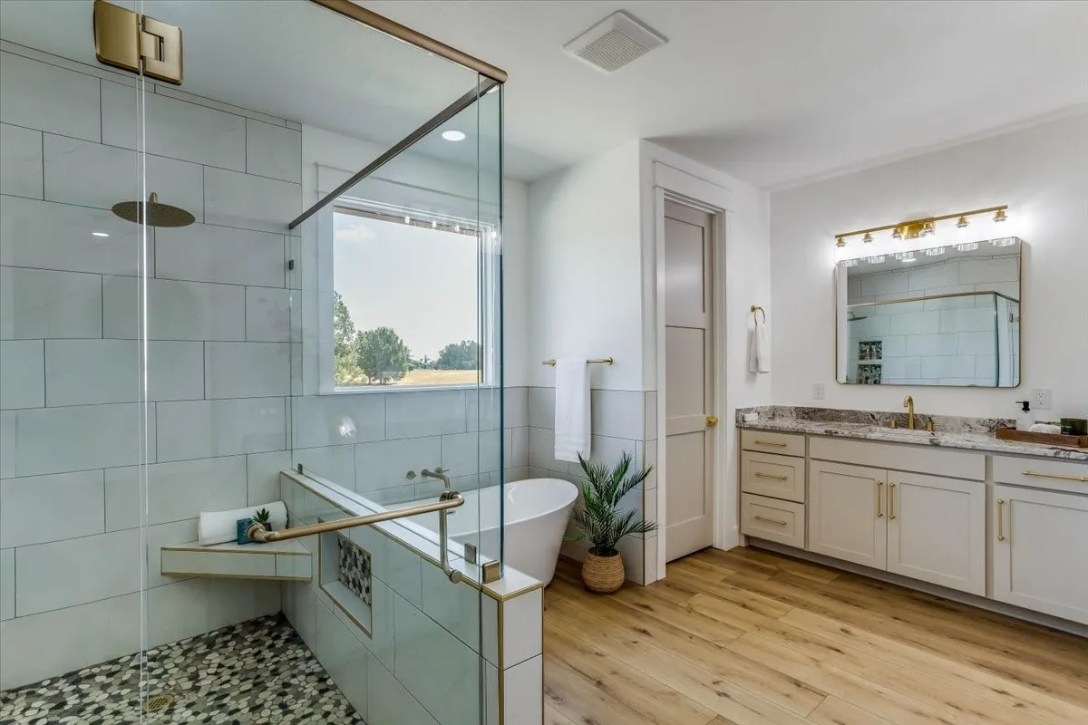 Walk-in shower with mosaic tile flooring, a freestanding soaking tub, a dual vanity with a stone countertop, and wood-finish flooring