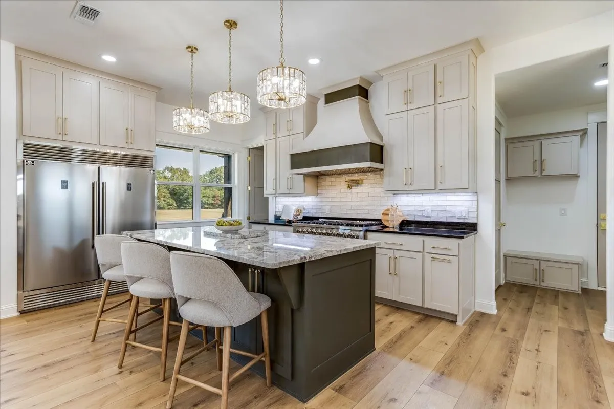 Gourmet kitchen featuring a large central island with seating, stainless steel appliances, a tile backsplash, light wood-finish flooring, and pendant lighting fixtures