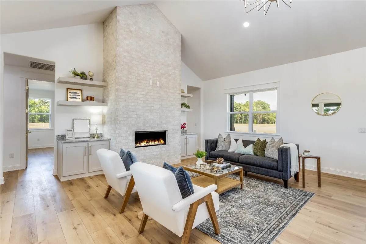 Vaulted ceiling with a contemporary chandelier, light wood-finish flooring, and a stone-clad fireplace with an integrated electric insert