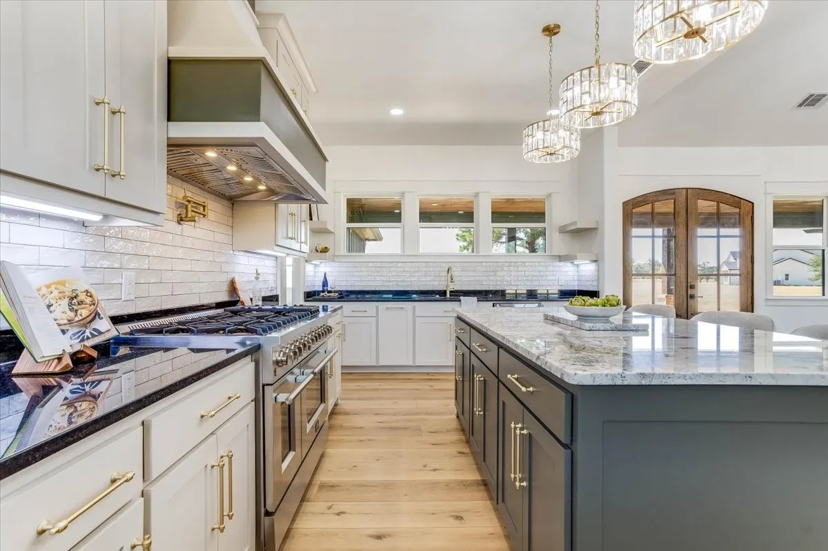 Gourmet kitchen featuring a large central island with light-toned countertop, stainless steel range with custom range hood, white subway tile backsplash, and light wood-finish flooring