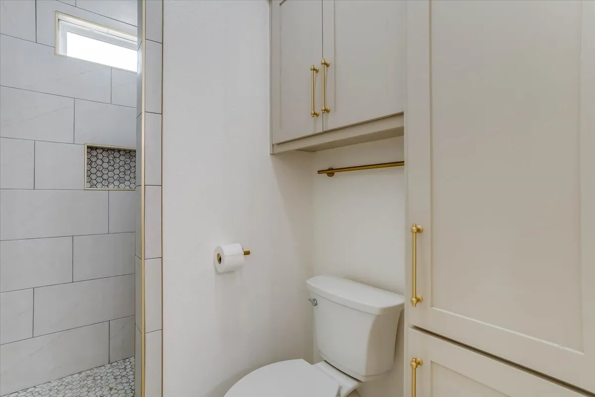 White tile shower with accent niche, pebble flooring, and transom window