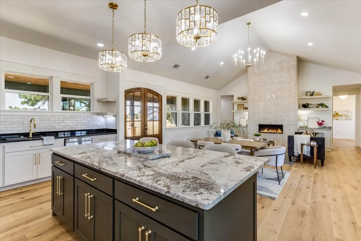 Open-concept living space with vaulted ceilings, a stone fireplace, wood-finish flooring, and a kitchen island with a granite countertop and pendant lighting