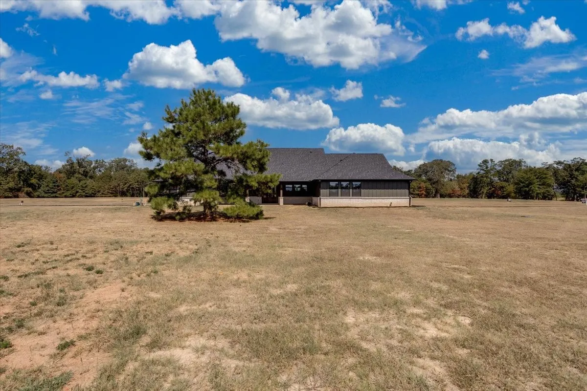 Expansive open field with a single mature tree, a dark-colored roof, and a visible foundation