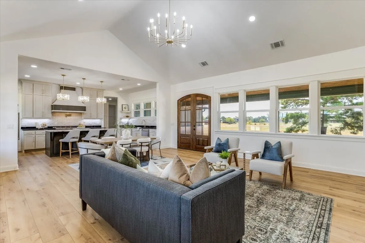 Vaulted ceiling with a chandelier, wood-finish flooring, kitchen island with counter seating, exposed wood double doors, and a wall of windows