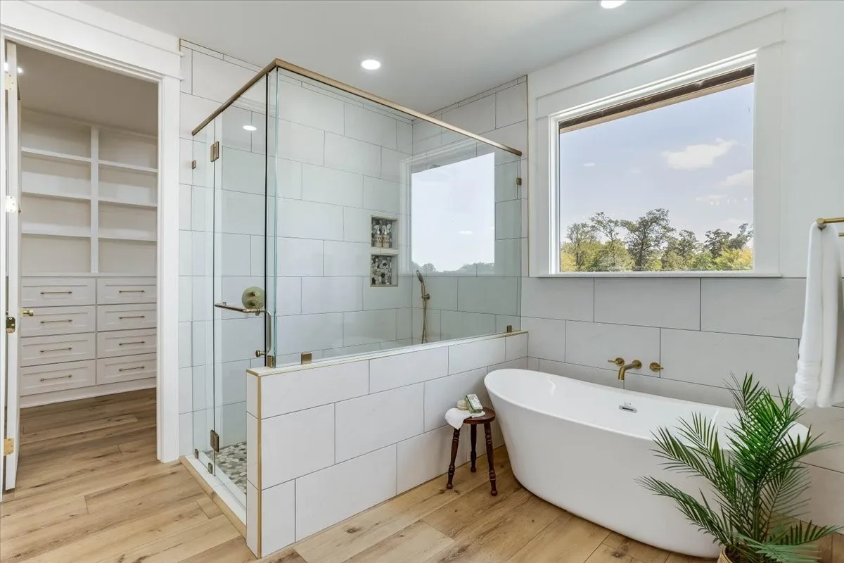 Wood-finish flooring, freestanding soaking tub, walk-in shower with glass enclosure, built-in shower niches, and built-in closet storage