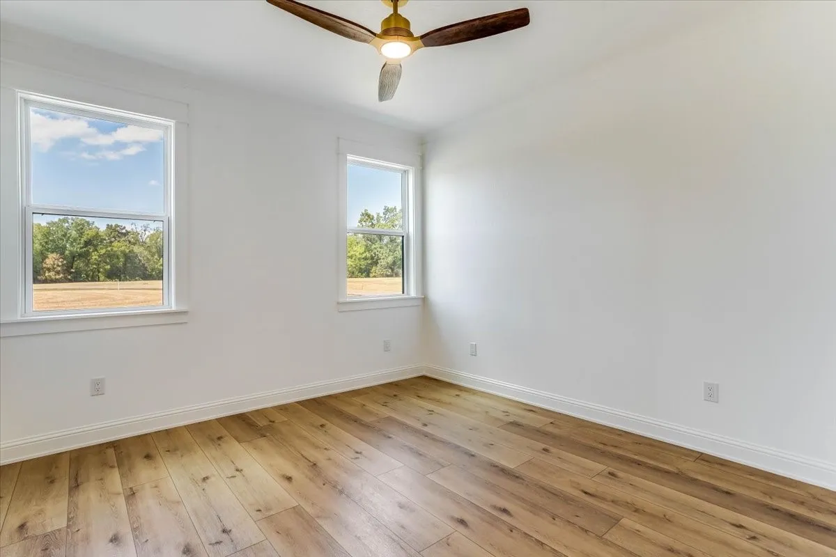 Two windows with white trim, wood-finish flooring, and a ceiling fan with wood blades